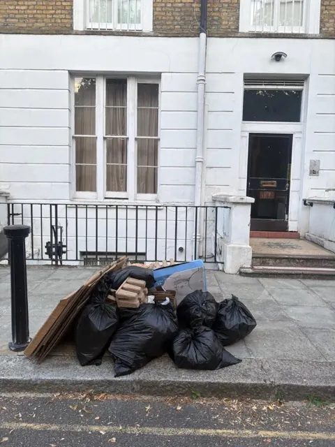 Before rubbish removal in Harlesden NW10 — black bags, cardboard and packaging piled on the pavement